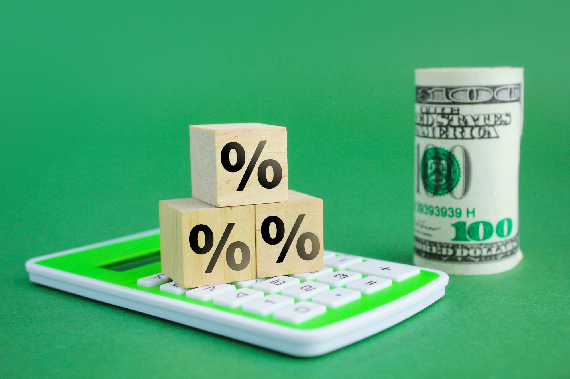 calculator, wooden cube with percent icon and a roll of money in blurred background