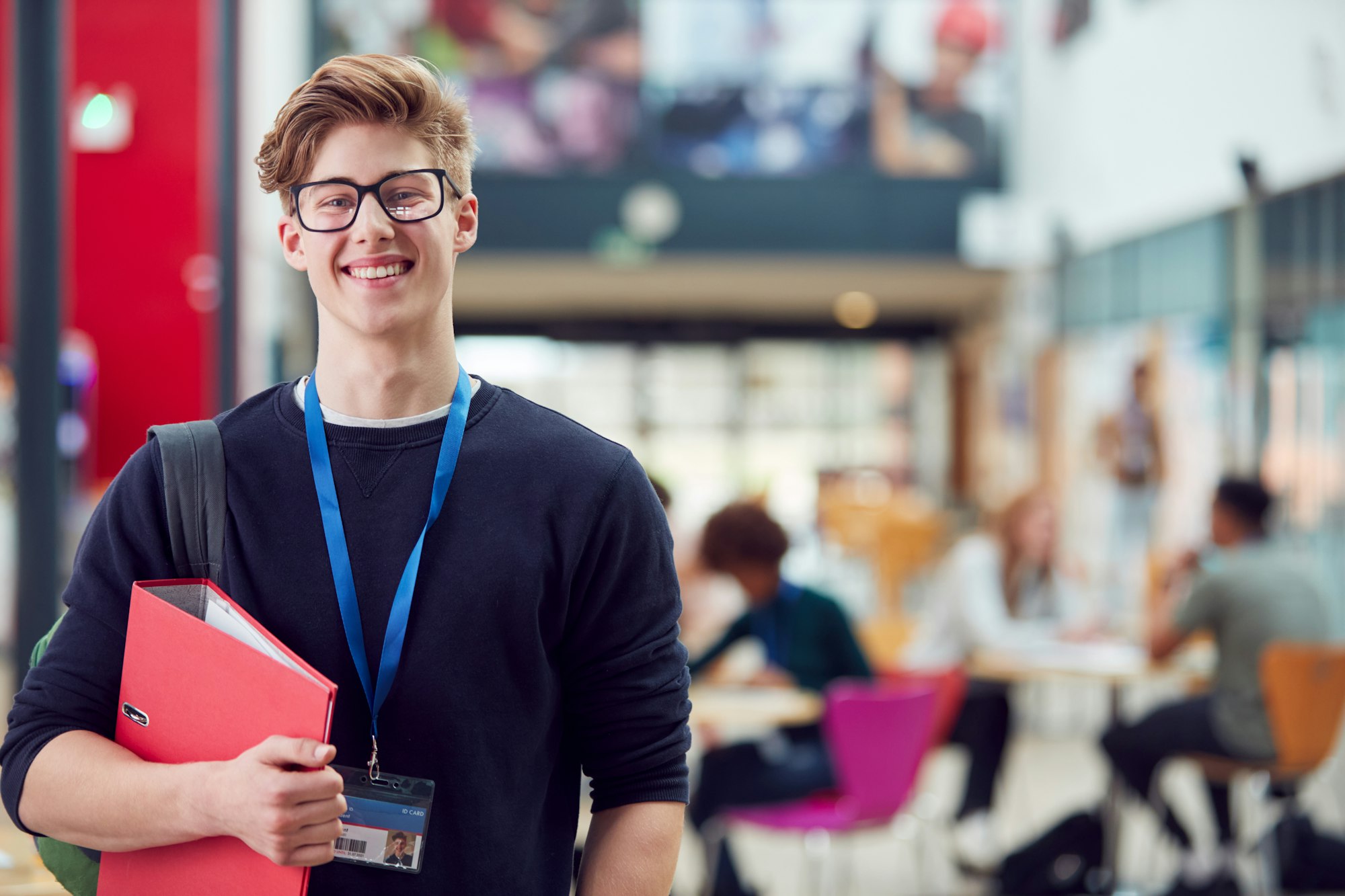 Portrait Of Smiling Male College Student In Busy Communal Campus Building